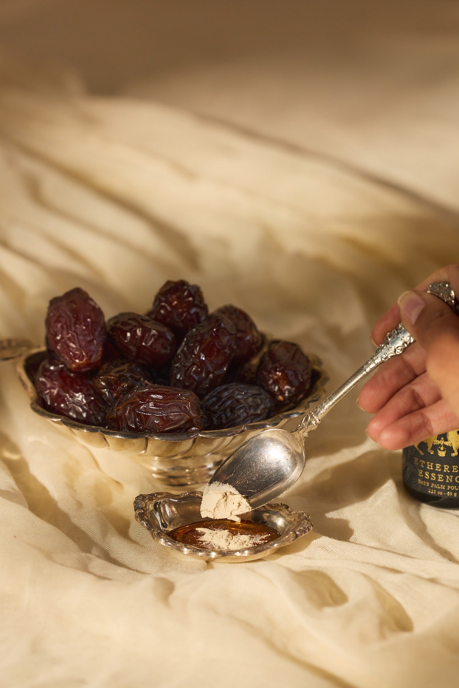 Bowl of dates with a spoon with Ethereal Essence on a textured surface.