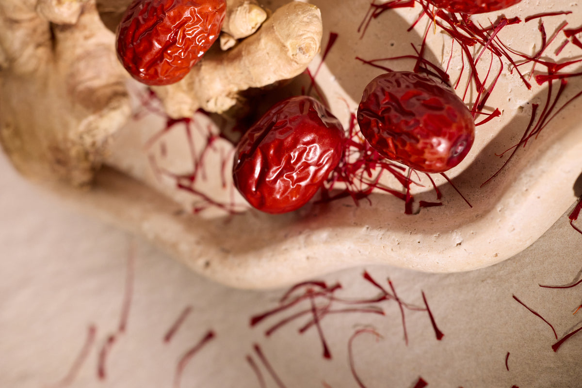 Dried red dates with saffron threads and ginger root on ceramic surface.