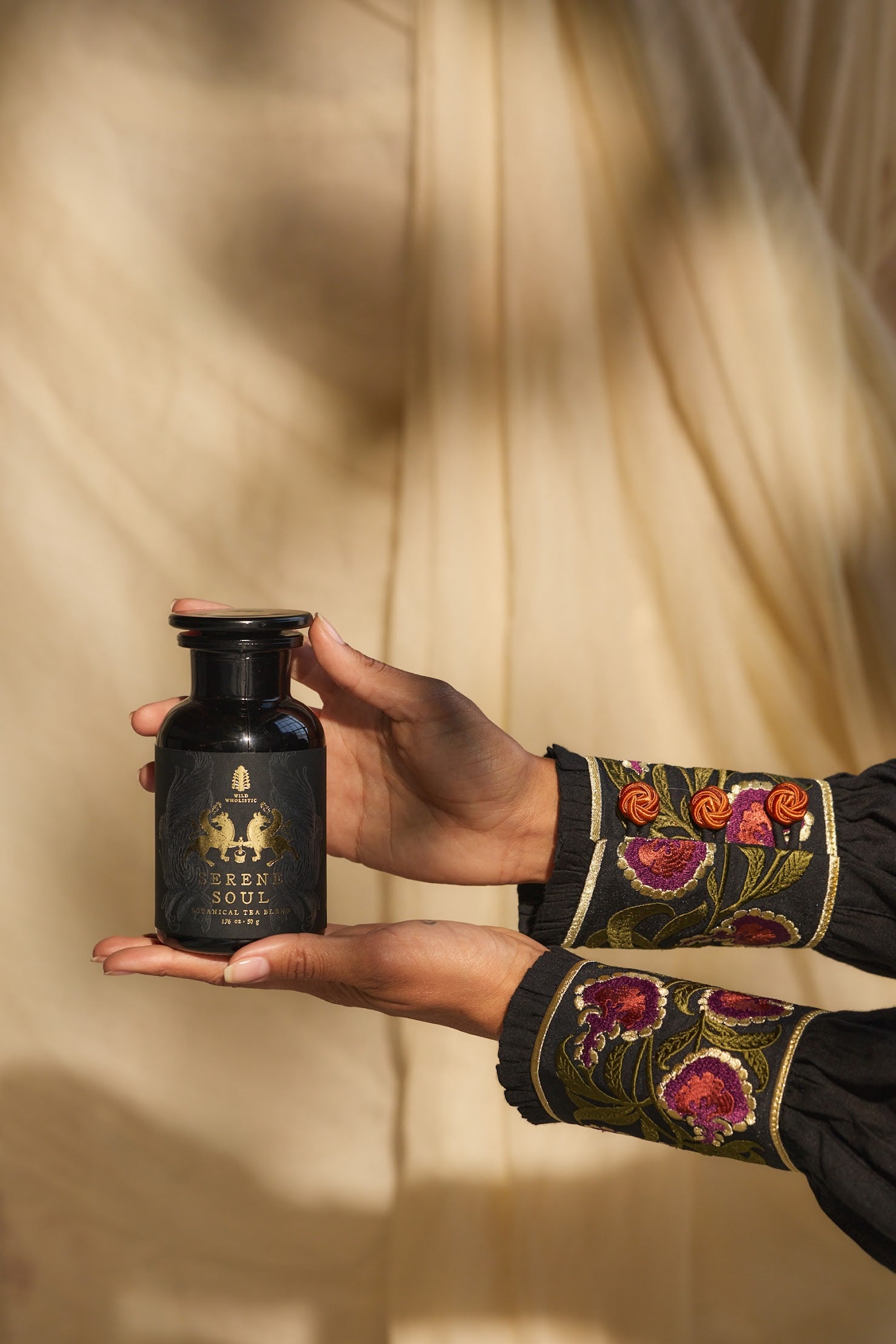 Hand holding a Serene Soul botanical tea blend in a black jar on a neutral background.